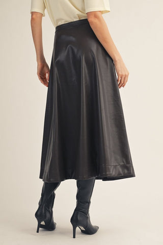 Black vegan leather A-line midi skirt with flared silhouette, styled with knee-high boots and cream top.