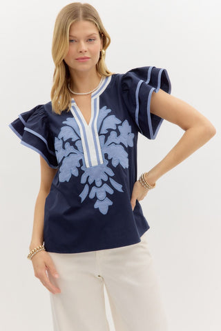 Navy flutter sleeve top with light blue floral appliqué design and striped V-neckline detail.
