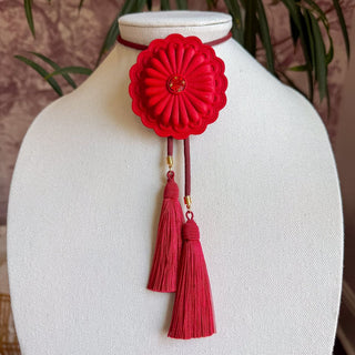 Red sculpted flower concho bolo tie with crimson pendant, dual maroon silk tassels, and gold accents.