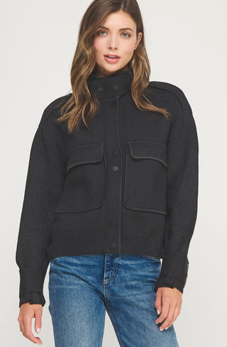 Black lurex knit jacket with satin piping trim, dual chest pockets, snap buttons, and mock neck collar.