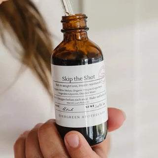 Hand holding amber glass dropper bottle of "Skip the Shot" herbal tincture by Evergreen Apothecary, Utah.