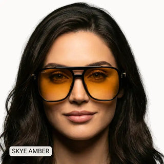 Unisex oversized aviator sunglasses with black frames and amber tinted lenses, modeled by dark-haired woman.