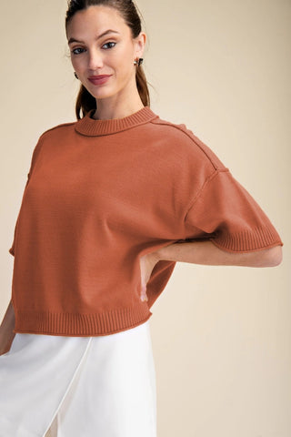Rust orange cropped mock-neck sweater with elbow-length sleeves, ribbed trim, and seam shoulder detail.