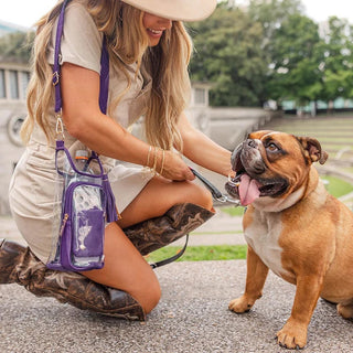 Clear stadium bag with purple trim and matching RFID pouch, worn crossbody by woman with bulldog outdoors.