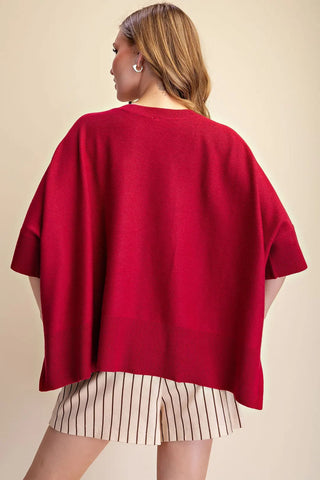 Red oversized pullover sweater with round neck and short sleeves, paired with striped shorts, back view.