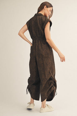 Woman wearing a sleeveless brown leopard print wide-leg jumpsuit with smocked waist and ruched hem detail.