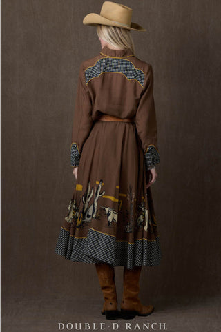 Woman wearing brown western shirt dress with desert scene print, checkered trim, belt, cowboy hat, and boots.