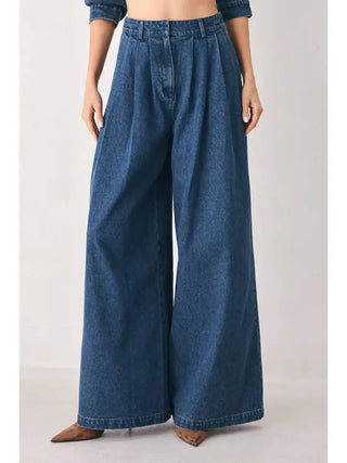 Medium blue wide-leg denim pants with pleated front, high waist, and dramatic flared silhouette.