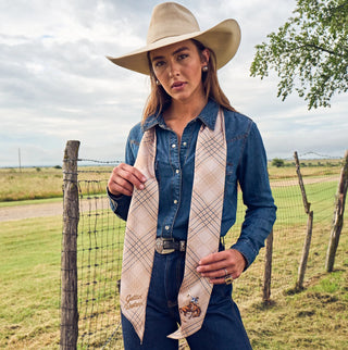 Tan and blue plaid western scarf tied around neck, worn with denim shirt and cowboy hat outdoors.