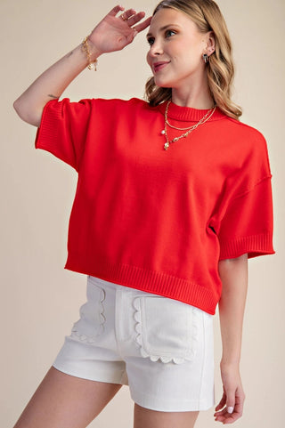 Red cropped mock-neck sweater with elbow-length sleeves and ribbed hem detailing, styled with white shorts.