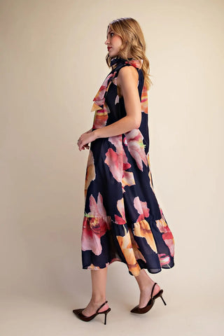 Navy blue sleeveless midi dress with bold watercolor floral print, ruffle neck tie, and tiered hem.