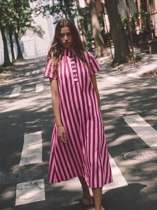 Pink and burgundy striped midi dress with stand collar, short sleeves, and button placket, worn outdoors.