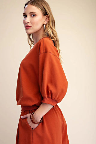 Rust orange pullover sweatshirt with puffed bubble sleeves, ribbed cuffs, and relaxed fit worn by blonde model.