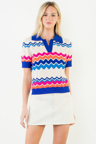 Short sleeve cream knit polo top with colorful blue, pink, and orange zigzag stripe pattern and blue collar.