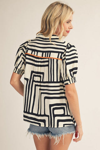 Black and white geometric print short sleeve top with orange contrast accent trim detail, back view.