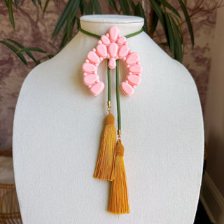 Blush pink arch-shaped bolo necklace with olive green cord and two golden yellow silk tassels.