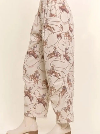 Cream relaxed crop pants with allover cowboy on horseback and lasso print, paired with white boots.