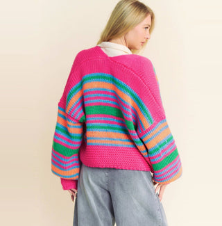 Chunky knit open cardigan with hot pink shoulders and multicolor striped body in green, blue, and orange.