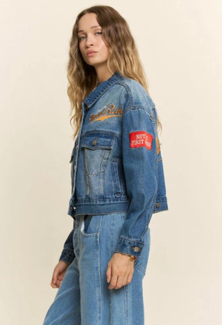 Medium wash cropped denim jacket with embroidered "Wild Ride" script and red patch on sleeve.
