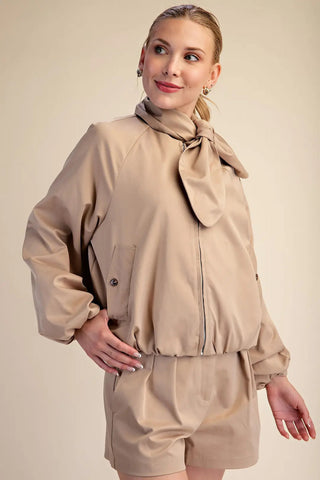 Beige puffy zip-front jacket with attached scarf collar tie, oversized silhouette, and elastic hem.