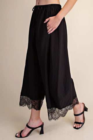 Black cropped wide-leg balloon pants with lace trim hem detail and elastic drawstring waistband.