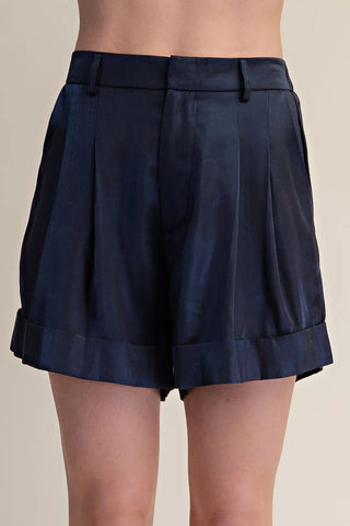 Navy blue satin pleated trouser shorts with cuffed hem and high waist on model.