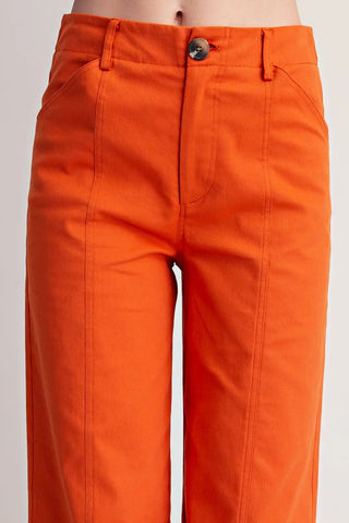 Orange wide leg pants with seam stitching detail, button closure, and front pockets, modeled at waist.