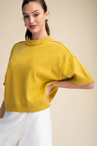 Mustard yellow cropped knit sweater with elbow-length sleeves, mock neck, and ribbed trim details.
