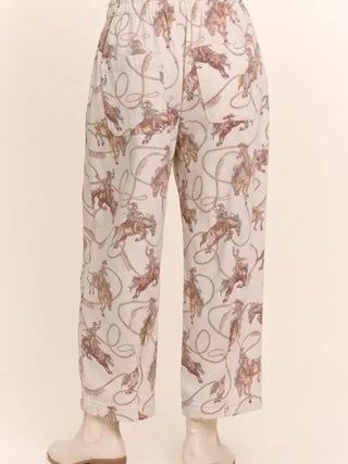 Cream relaxed crop pants featuring allover rodeo cowboy and horse print with lasso rope details.