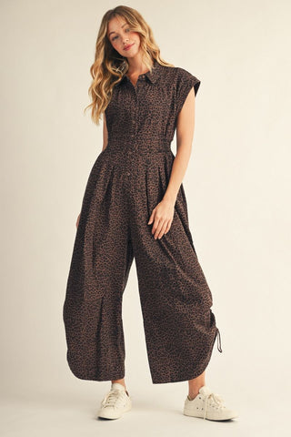 Brown leopard print wide-leg jumpsuit with drop shoulders, button front, smocked waist, and white sneakers.