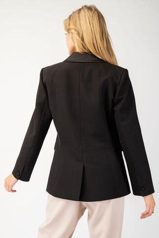Black long sleeve satin collar blazer jacket with button cuffs and center back vent, rear view.