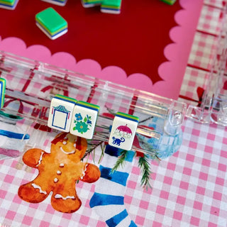 Pink gingham mahjong mat featuring gingerbread men and Christmas stockings with clear tile racks and colorful tiles.