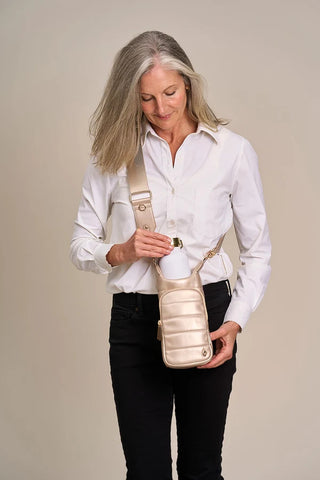 Woman wearing a soft gold vegan leather crossbody HydroBag with matching wide shoulder strap, holding white water bottle.