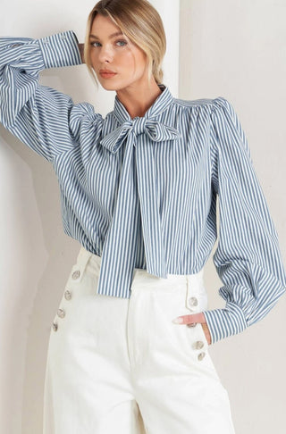 Blue and white striped woven blouse with bow neck tie, puff sleeves, and button front detailing.