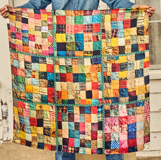 Colorful handmade patchwork crazy quilt featuring multicolored fabric squares with teal zigzag sash borders, held up by perso