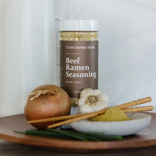 A 11.7 oz jar of Clean Monday Meals Beef Ramen Seasoning surrounded by onion, garlic, chives, and chopsticks.