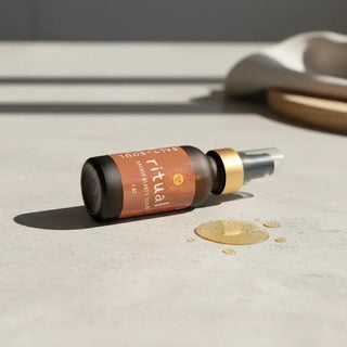 Frosted dark glass dropper bottle of Salt Soul Ritual Sacred Beauty Serum lying on its side on a light stone surface, with go