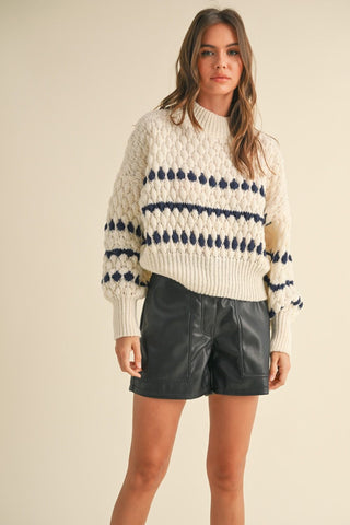 Cream chunky knit sweater with navy blue dot and stripe pattern, paired with black leather shorts.