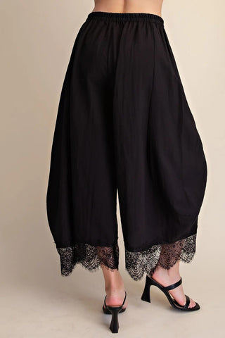 Black cropped balloon pants with elastic waistband and decorative lace trim hem detail, styled with black heels.