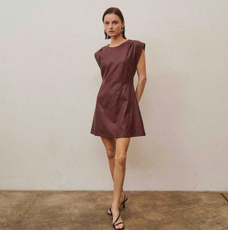 Burgundy vegan leather mini dress with cap sleeves, A-line silhouette, and crew neckline, styled with strappy heels.