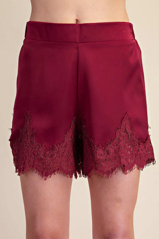 Burgundy satin shorts with elegant floral lace trim detail along scalloped hemline, high waist style.