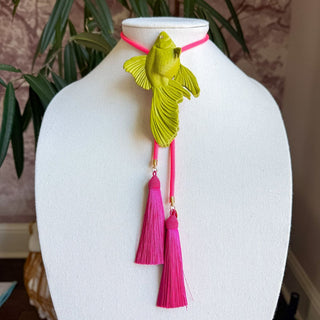 Olive green goldfish bolo necklace with neon pink cord and two fuchsia silk tassels on jewelry display bust.