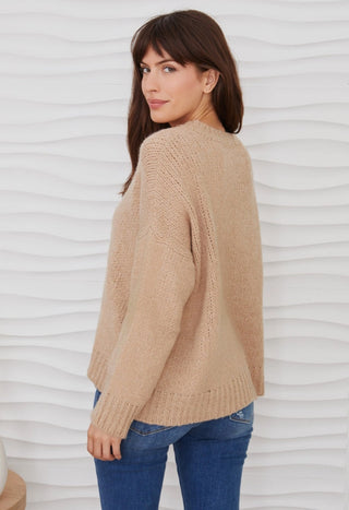 Woman wearing a camel beige fuzzy knit long sleeve V-neck sweater with blue jeans, back view.