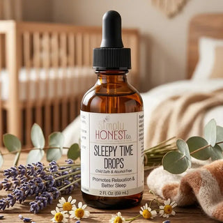 Amber dropper bottle of Simply Honest Co. Sleepy Time Drops surrounded by lavender and chamomile flowers on wooden surface.