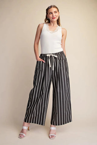 Black and white vertical stripe wide leg pants with cream drawstring waistband and side pockets.
