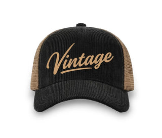 Black corduroy trucker hat with tan mesh back panels and gold "Vintage" script logo on front panel.