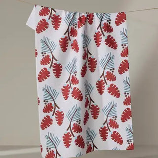 White tea towel printed with red pinecones and blue pine branches, hung on a line.