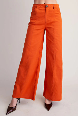 Orange wide-leg pants with seam stitching detail, high waist, single button closure, styled with brown heels.