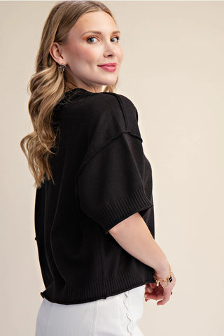 Black knit sweater with elbow-length sleeves, seam detail, and ribbed hem worn by blonde model.