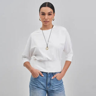 White 3 quarter sleeve relaxed fit top worn with blue jeans and gold hoop earrings.